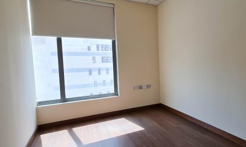 An empty room with stunning wooden floors and a window available for rental in Seef.