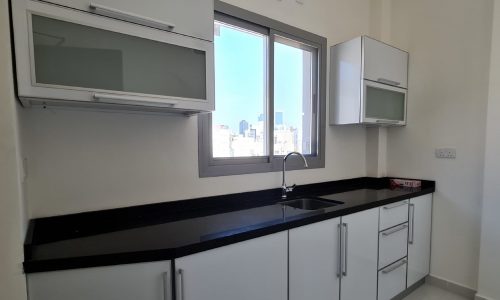 A kitchen with white cabinets and black counter tops available for rent in Seef.