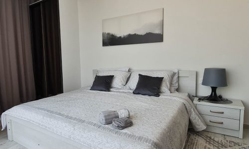 A luxury studio for rent in Seef with a stunning sea view and a white bed adorned with a painting on the wall.