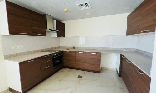 A modern kitchen with wooden cabinets and white counter tops in a bright and flat for sale.
