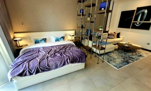 A luxury bedroom with a bed and a bedside table in a 5-star serviced apartment for sale in Juffair.