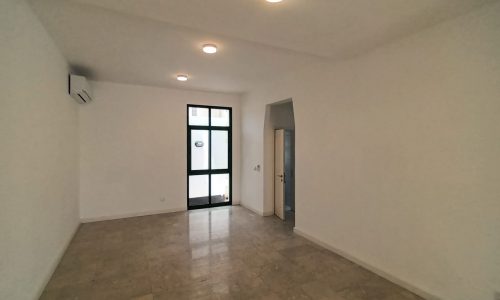 A spacious commercial villa for rent in Adliya with an empty room featuring white walls and a ceiling fan.