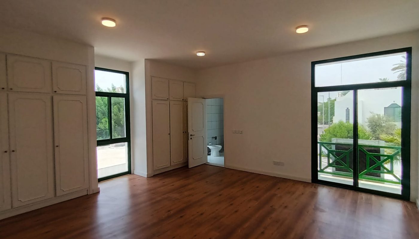 A commercial villa in Adliya, available for rent. The villa features an empty room with wood floors and sliding glass doors.