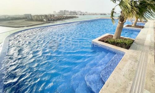 A swimming pool with palm trees and a sea view.