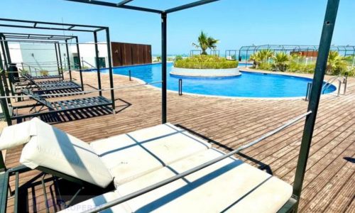 An amazing wooden deck with lounge chairs and a swimming pool, perfect for enjoying the sea view from your apartment.