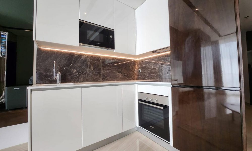 A modern studio kitchen with white cabinets and marble countertops, located in Water Garden City.