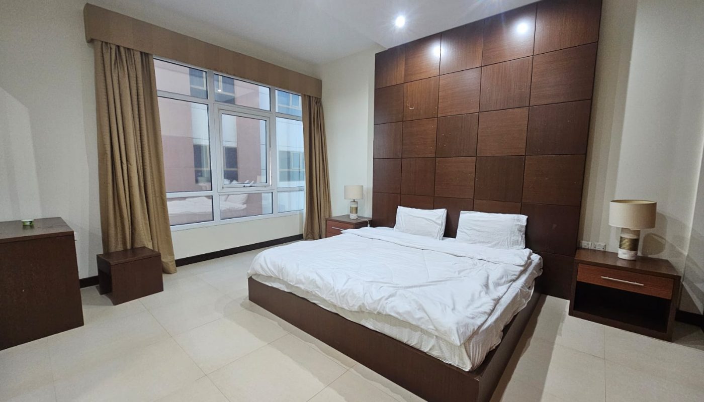 A flat in Juffair available for rent. The flat features a bedroom with a bed and a large window.