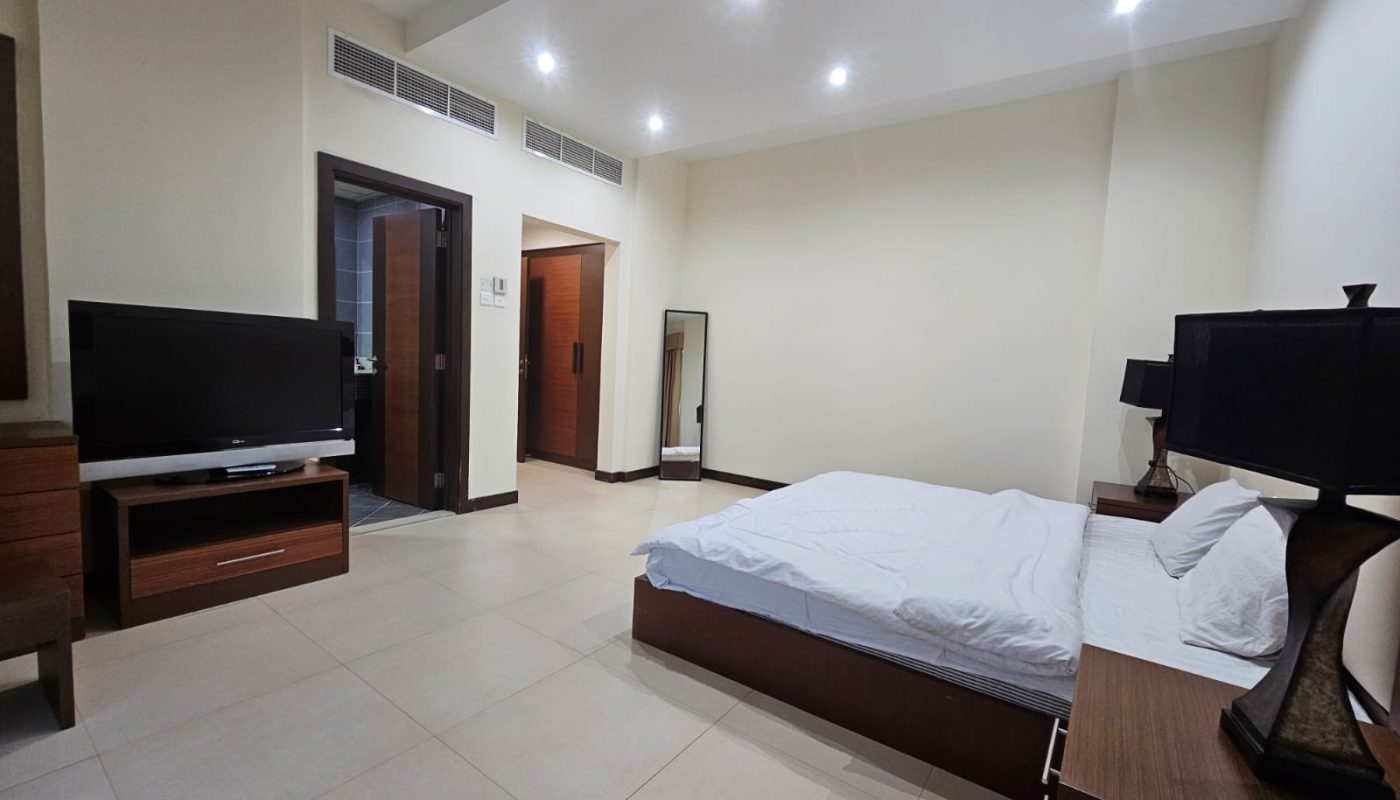 Rent: A Juffair flat with a bedroom equipped with a bed, tv, and a bedside table.