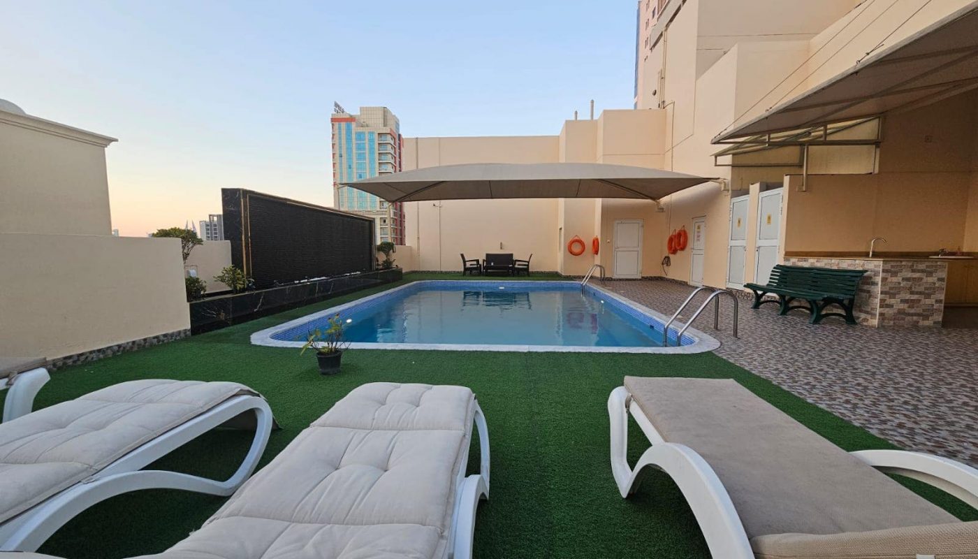 A rooftop swimming pool and lounge chairs on a flat building available for rent in Juffair.