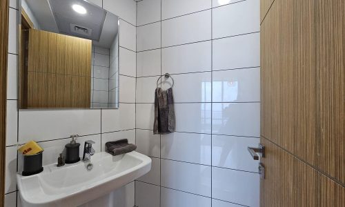 A white bathroom with a sink and mirror available for rent in the Seef area.