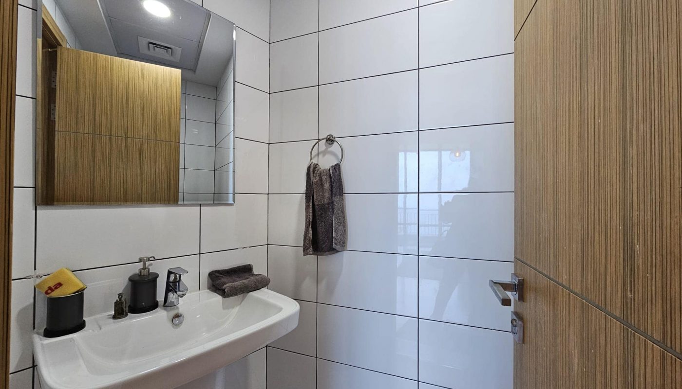 A white bathroom with a sink and mirror available for rent in the Seef area.