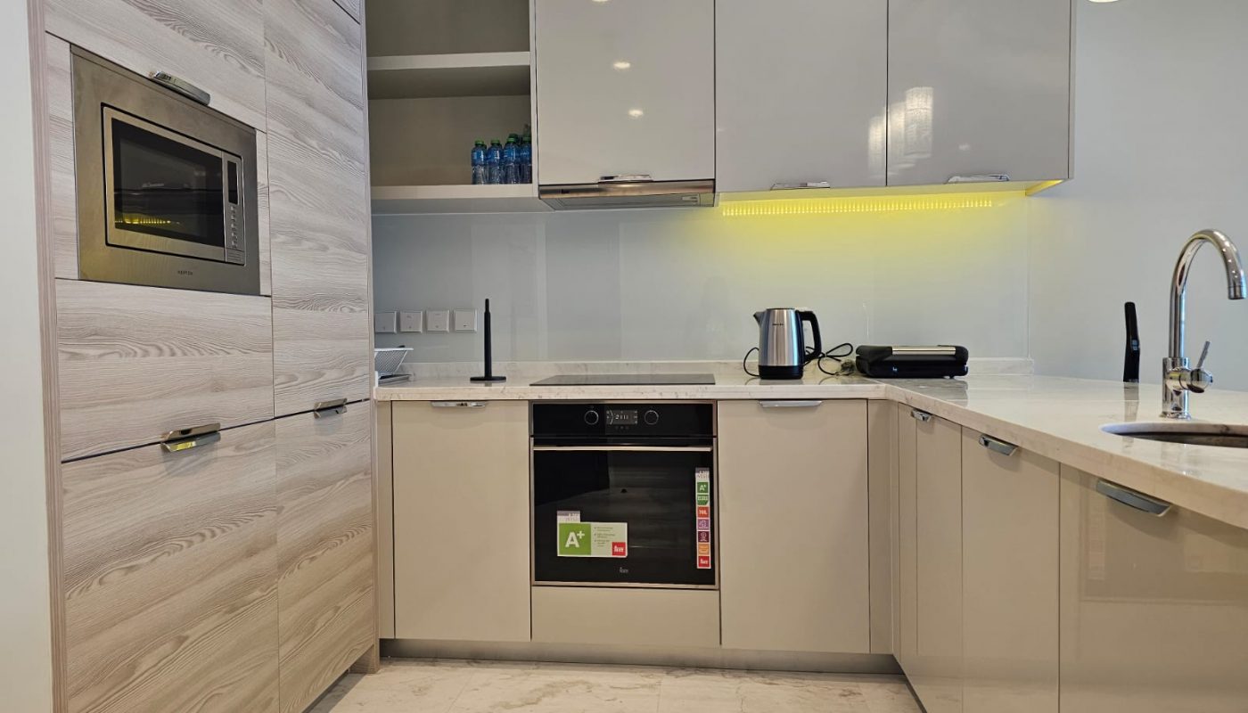 Rent a modern flat in Al Manama with a contemporary kitchen featuring white cabinets and marble counter tops.