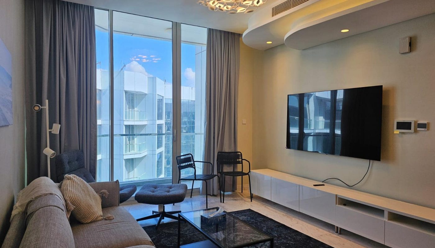 A rentable flat in Al Manama with a living room, TV, and an ocean view.