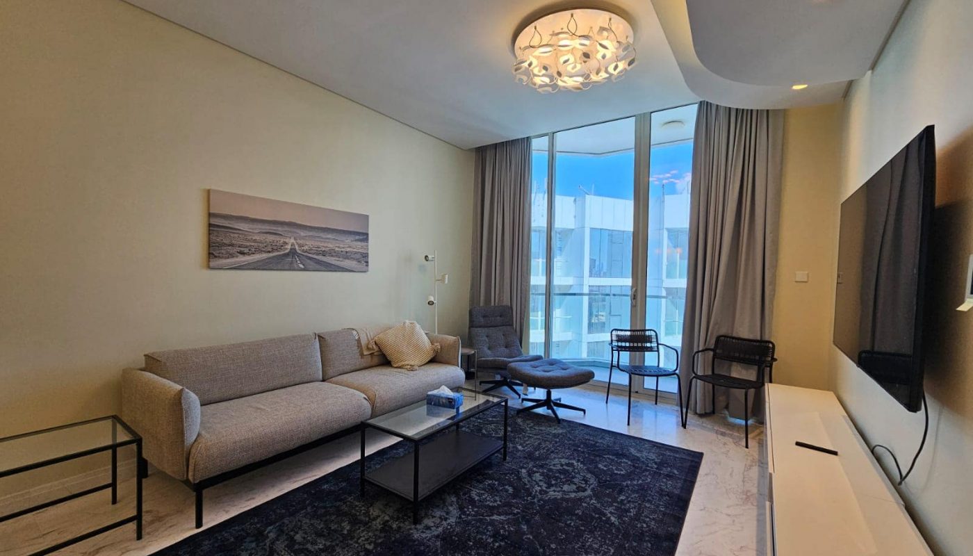 A flat in Al Manama available for rent, featuring a living room with a flat screen tv and a couch.