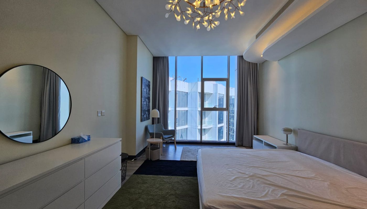 A spacious bedroom in a flat for rent in Al Manama, featuring a large bed and a large mirror.
