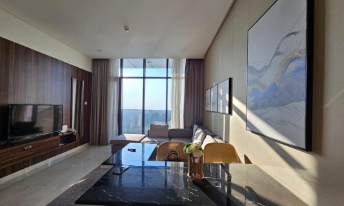 Modern living room in a fully-furnished one-bedroom apartment with large windows, a marble table, brown chairs, wooden cabinets, a television, and a large framed artwork on the wall.