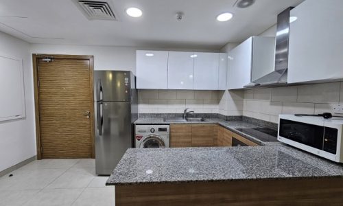 A kitchen with stainless steel appliances and wooden cabinets in a flat for rent in Juffair.