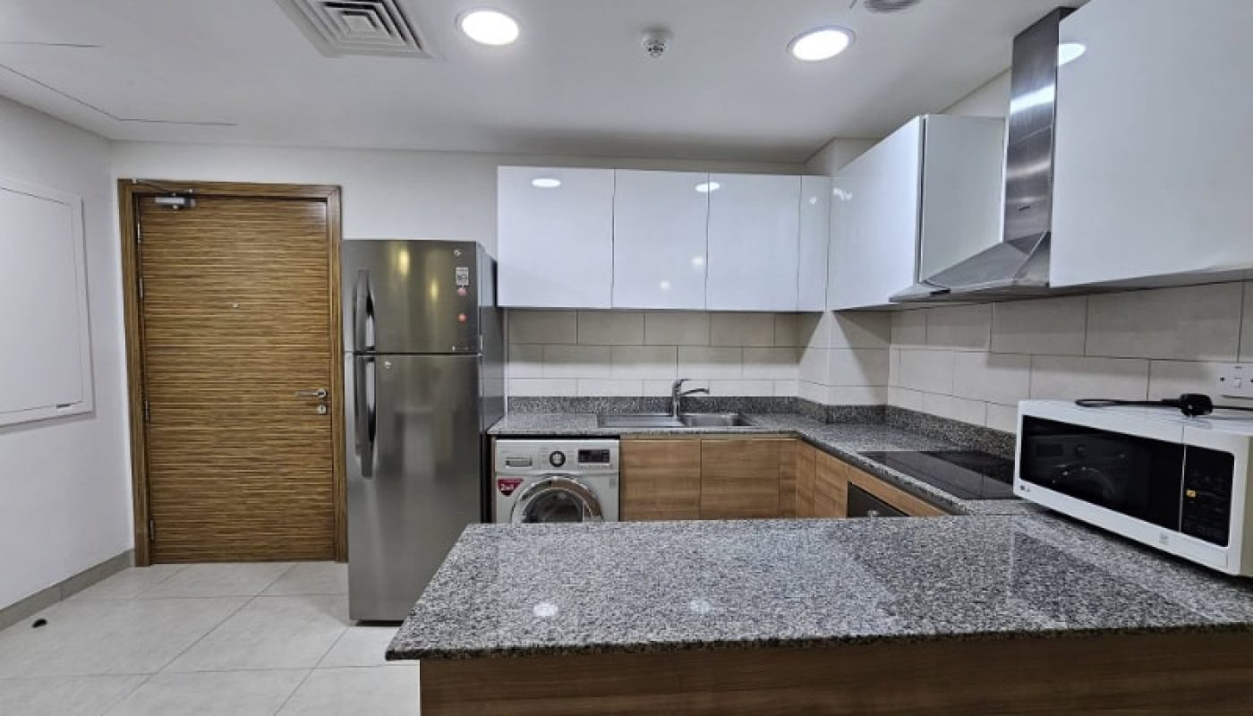 A kitchen with stainless steel appliances and wooden cabinets in a flat for rent in Juffair.