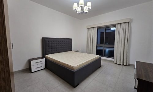 A bedroom with a bed and a dresser for rent in Juffair.