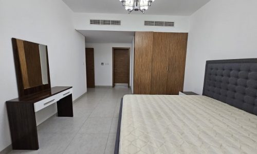 A bedroom for rent in Juffair with a bed, dresser, and mirror.