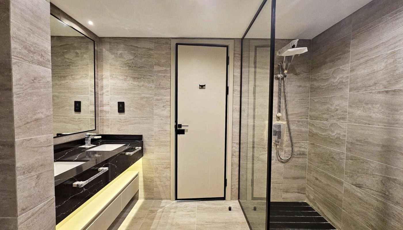 Modern bathroom interior with a walk-in shower, glass partition, wall-mounted sink, and large mirror.