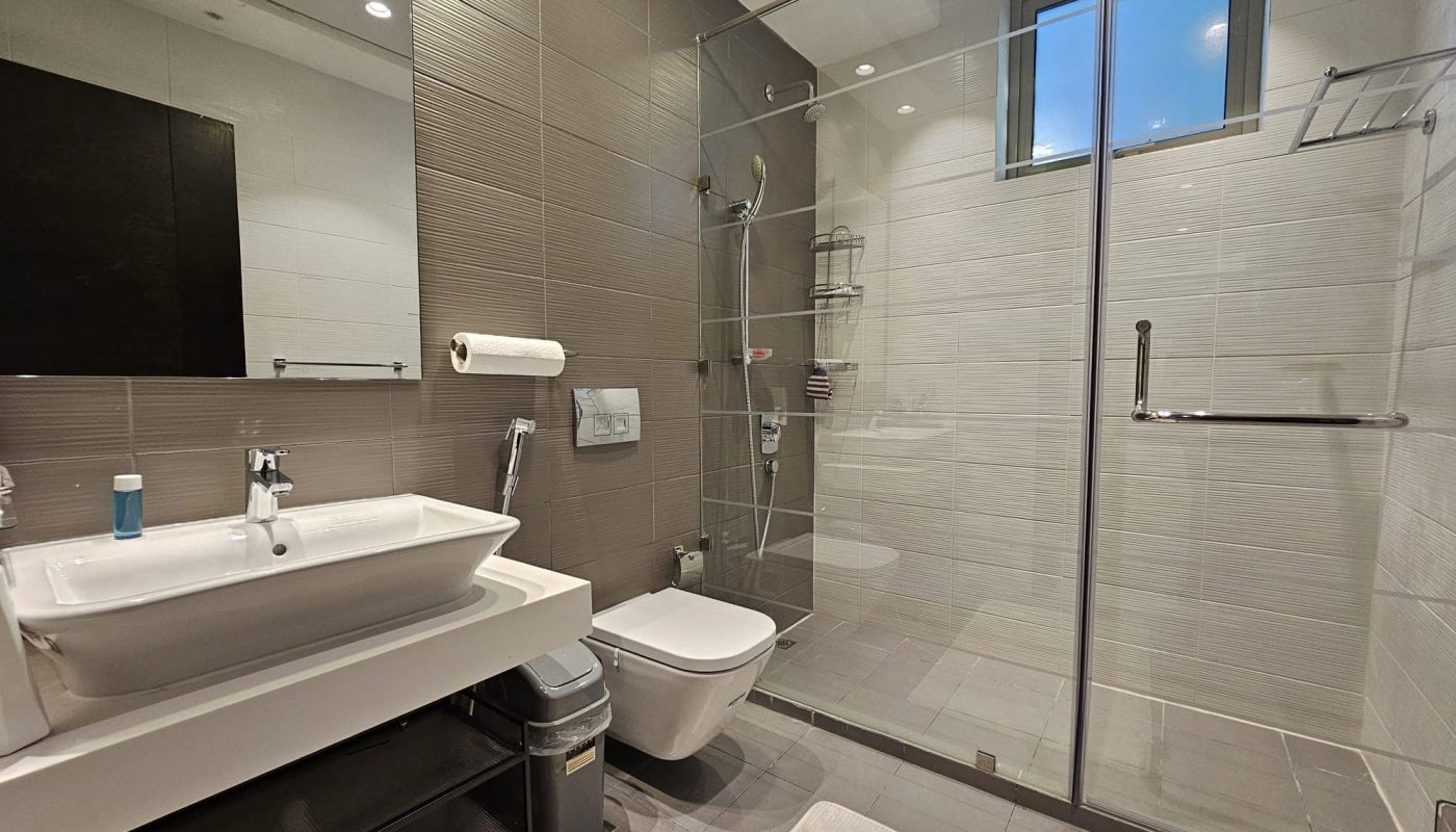 Modern bathroom interior with glass shower enclosure, white basin, auto draft system, and tiled walls.