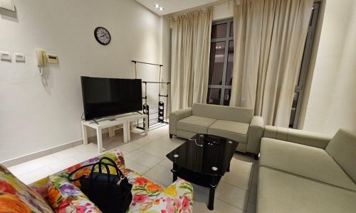 A modern living room interior at night with a flat-screen tv, a beige sofa, a colorful armchair, and glass center tables is available for rent in Seef.