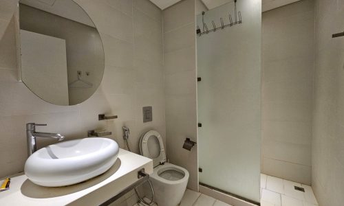 A modern bathroom interior in a flat for rent, featuring a wall-mounted basin, toilet, and glass shower enclosure.