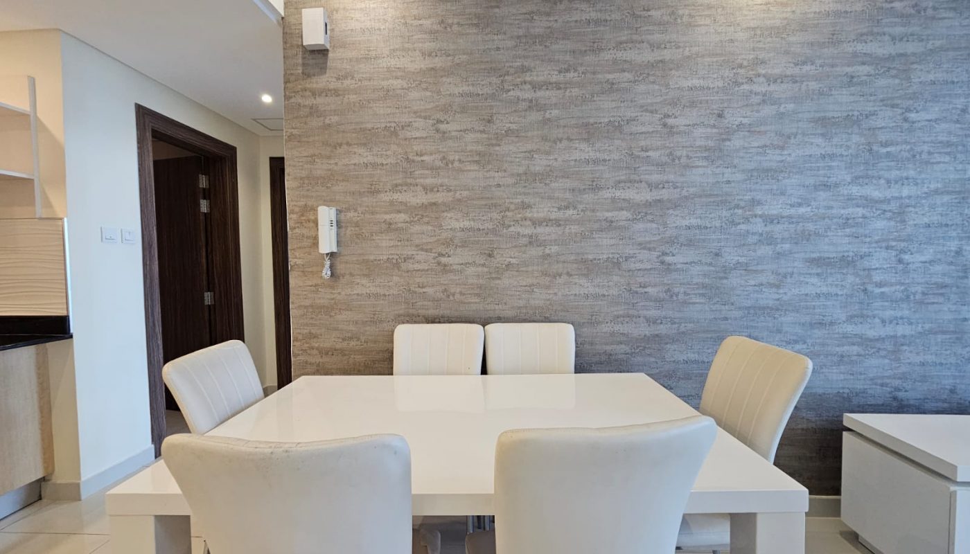Luxury apartment for rent featuring a modern dining area with a white table, four chairs, and textured gray wall in Juffair.