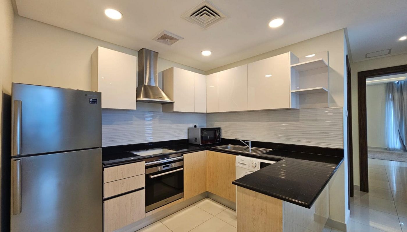 Modern kitchen interior in a luxury apartment for rent, with stainless steel appliances, white cabinetry, and a tiled backsplash.