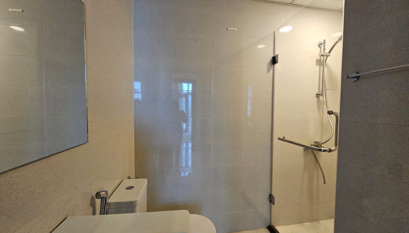 Luxury apartment bathroom interior for rent in Juffair, featuring a glass shower enclosure, wall-mounted toilet, and sink.
