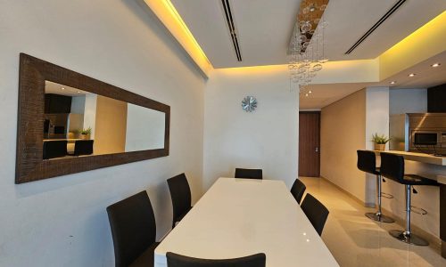 Modern dining room with white table, black chairs, and a kitchen bar area.