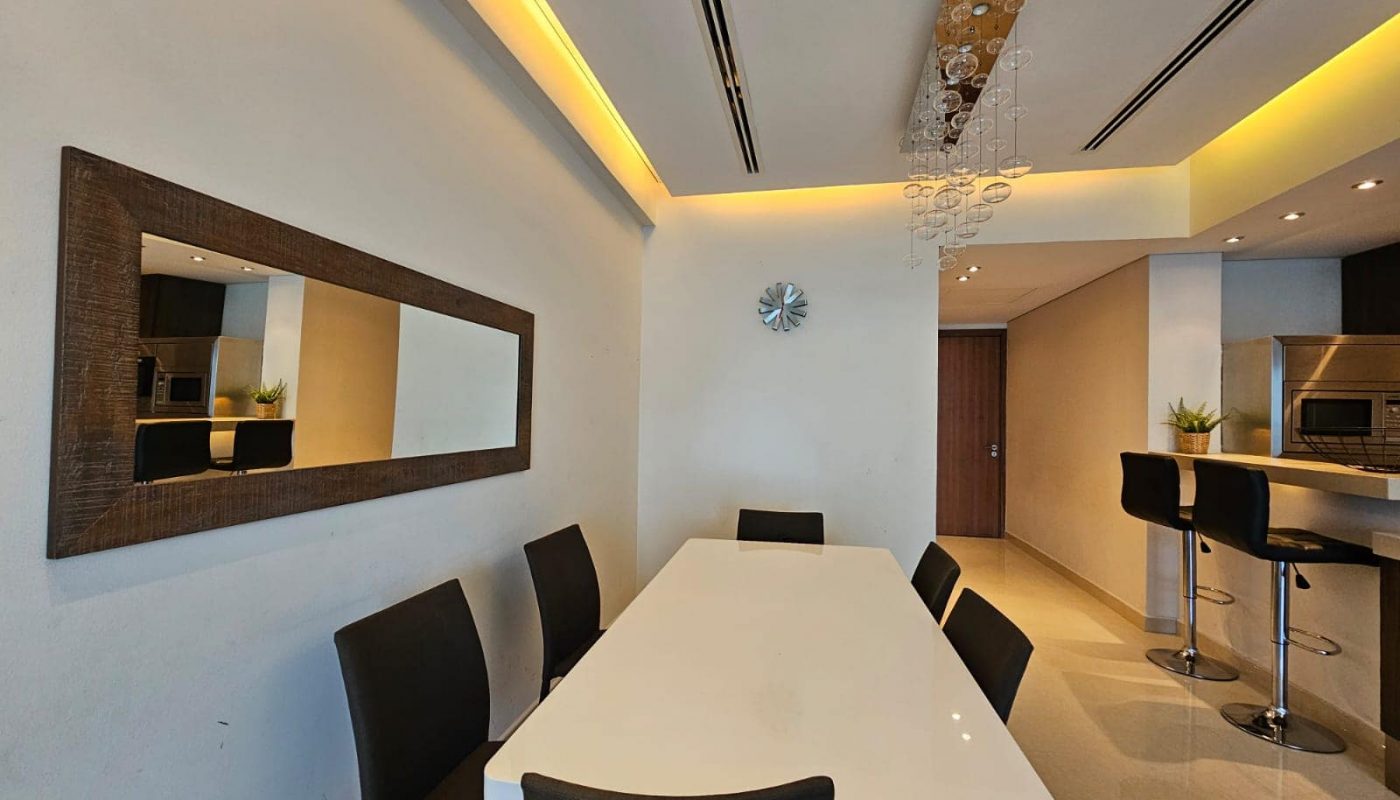 Modern dining room with white table, black chairs, and a kitchen bar area.