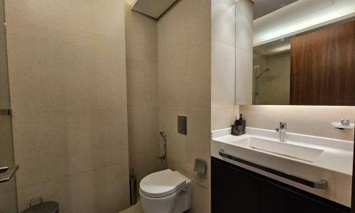 Modern bathroom interior with beige tiles, featuring a toilet, wash basin with vanity, and a mirror.