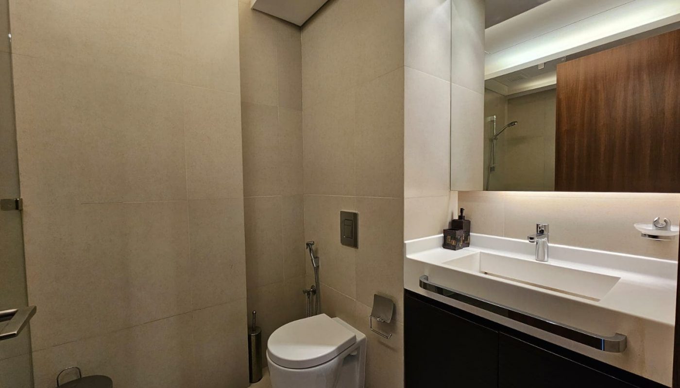 Modern bathroom interior with beige tiles, featuring a toilet, wash basin with vanity, and a mirror.