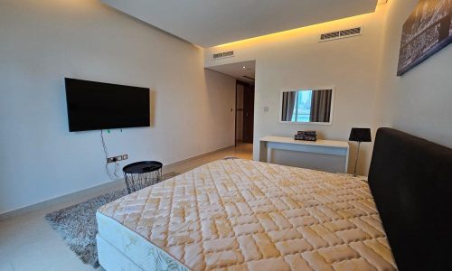 Modern bedroom interior with a large bed, wall-mounted tv, and minimalistic decor.