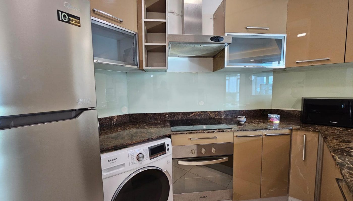 Luxurious apartment with modern kitchen interior, stainless steel appliances, and open wooden cabinets for rent in Juffair.