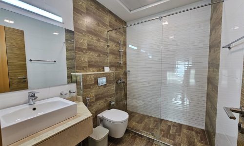 Luxurious modern bathroom interior with glass shower cabin, wooden tiles, and white sanitary ware.