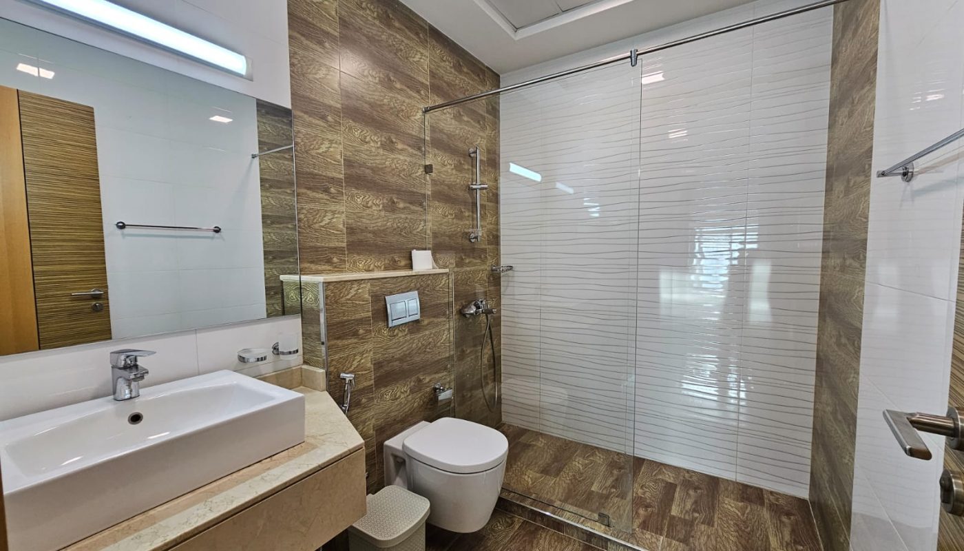Luxurious modern bathroom interior with glass shower cabin, wooden tiles, and white sanitary ware.