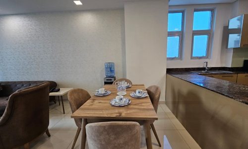 Modern kitchen with dining area featuring a wooden table set for four, a brown sofa, and an auto draft water cooler near a window.