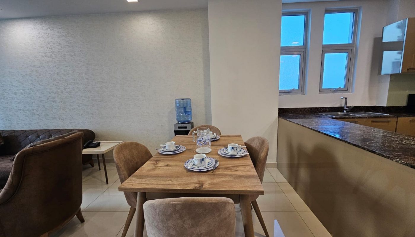 Modern kitchen with dining area featuring a wooden table set for four, a brown sofa, and an auto draft water cooler near a window.