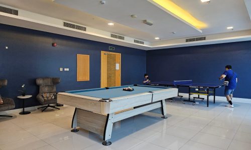 A recreational room with blue walls, featuring a pool table and a ping pong table, with two individuals playing ping pong in the background. Auto Draft