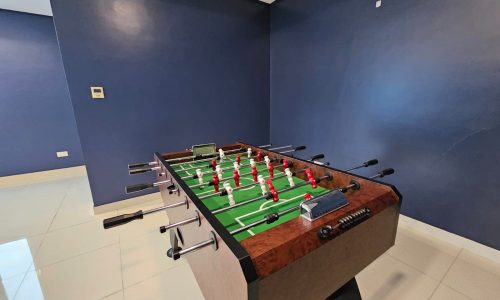 A foosball table in a room with dark blue walls and a tiled floor, equipped with an auto draft.