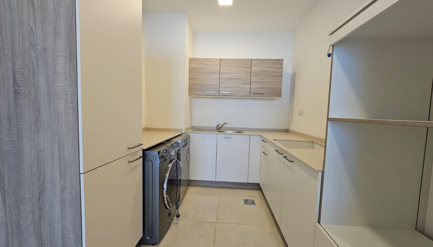 A modern, empty kitchen with white cabinetry and built-in appliances in a luxury apartment for rent in the Juffair area.