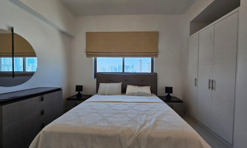 Modern bedroom interior with a large bed, city view window, and sleek furniture.