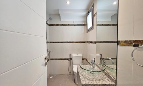 Modern 3 bedroom, fully-furnished flat in Juffair with a bathroom interior including a glass sink, toilet, and wall-mounted mirror.