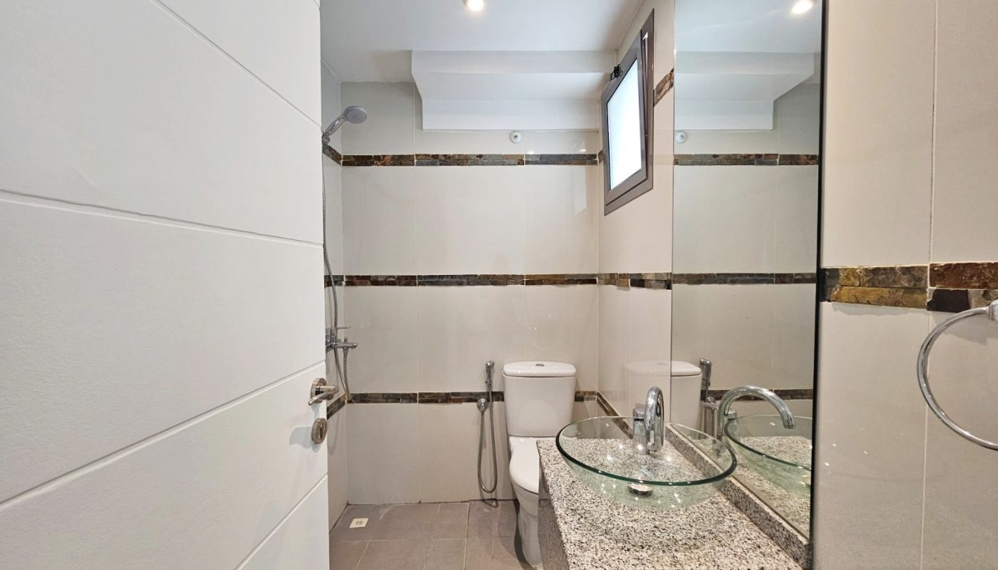 Modern 3 bedroom, fully-furnished flat in Juffair with a bathroom interior including a glass sink, toilet, and wall-mounted mirror.