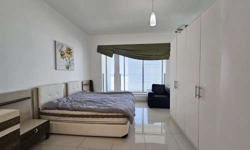 Bright, modern 3-bedroom fully-furnished flat in Juffair with a large bed, tiled floor, and a window draped with a green curtain.