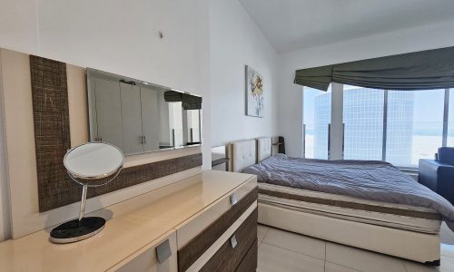 Modern 3 bedroom flat with a large bed, vanity mirror, and floor-to-ceiling window with city view.