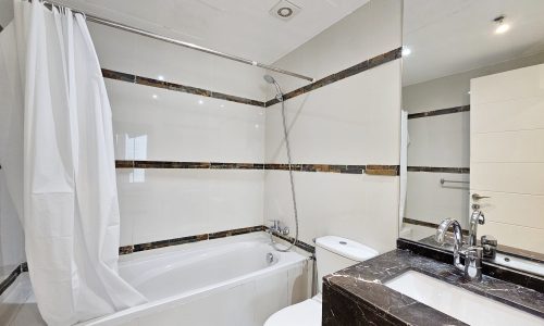 Modern 3-bedroom bathroom interior in Juffair with a bathtub, shower, toilet, and marble countertop.